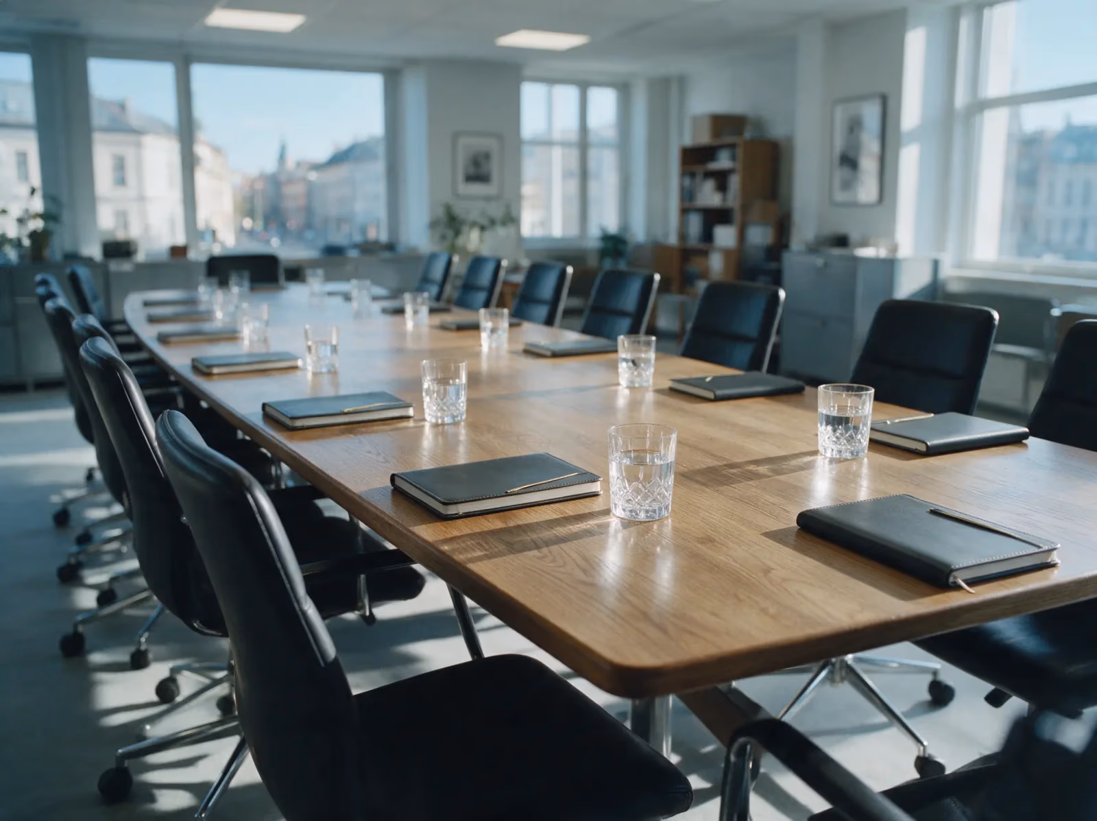 An empty boardroom table set for a meeting, a notebook and a glass of water at each seat